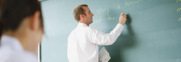  Profesor con camisa blanca escribiendo con tiza amarilla sobre pizarra verde 