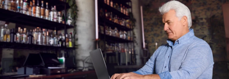  Un hombre mayor está usando una computadora portátil en un bar. 