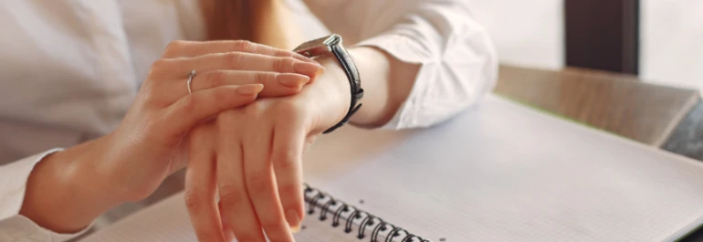  Una persona revisa su reloj mientras está sentada frente a una libreta. 
