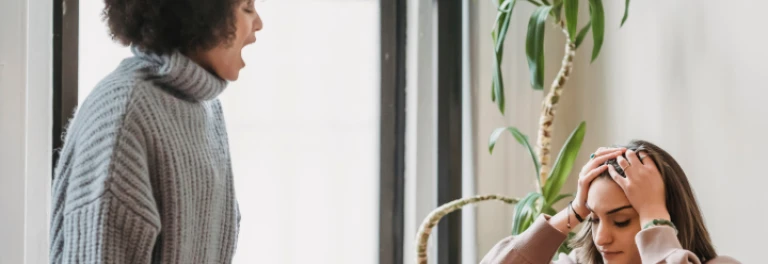  chica con pelo rizado gritándole a chica sujetándose la cabeza 
