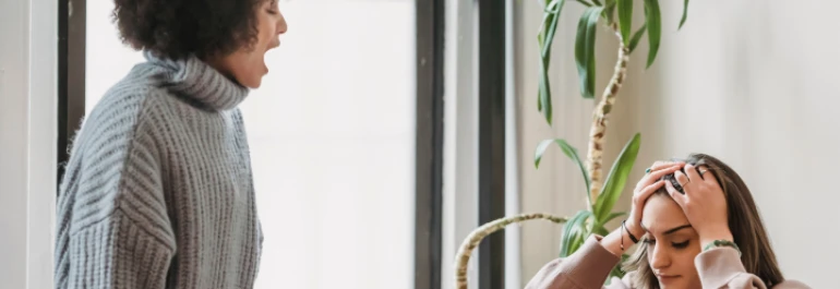  chica con pelo rizado gritándole a chica sujetándose la cabeza 