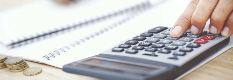  Una mano usando una calculadora junto a unas monedas y un cuaderno. 