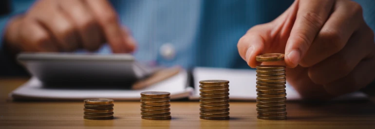  Persona calculando con montones de monedas encima de la mesa 