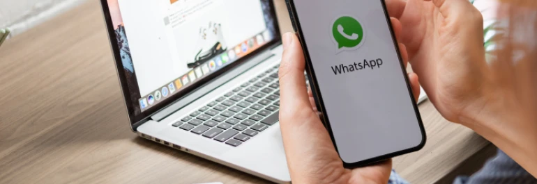  Una persona sostiene un teléfono que muestra la aplicación de WhatsApp, frente a una laptop. 