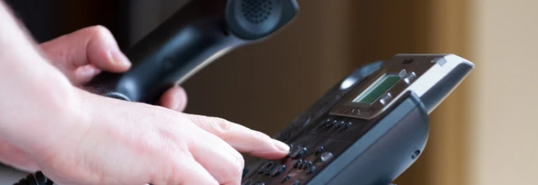  Una persona está marcando un número en un teléfono fijo mientras sostiene el auricular. 