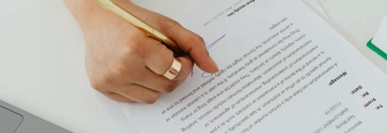  Una mano firmando un documento con un bolígrafo dorado. 