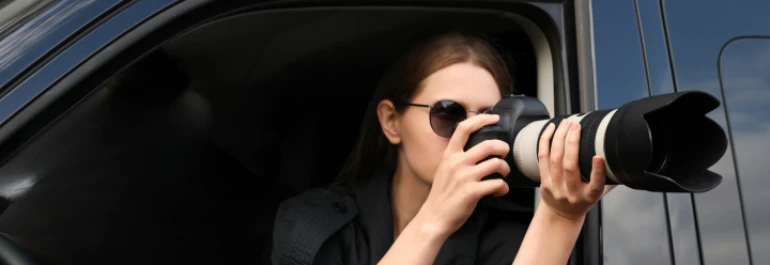  Una persona con gafas de sol está tomando fotos con una cámara de lente largo desde un automóvil. 