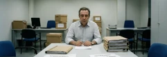  Trabajador en oficina vacía frente a despido y con cajas de documentos en el fondo 