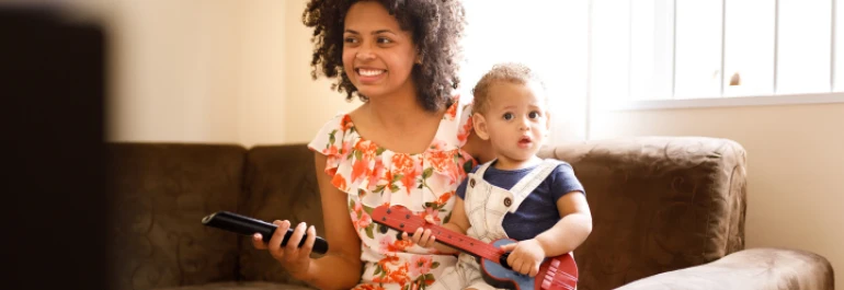  Una mujer sonríe mientras sostiene un control remoto junto a un niño pequeño que tiene una guitarra de juguete. 