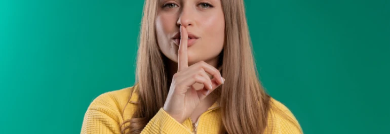  Una mujer con suéter amarillo hace el gesto de silencio con el dedo en los labios. 