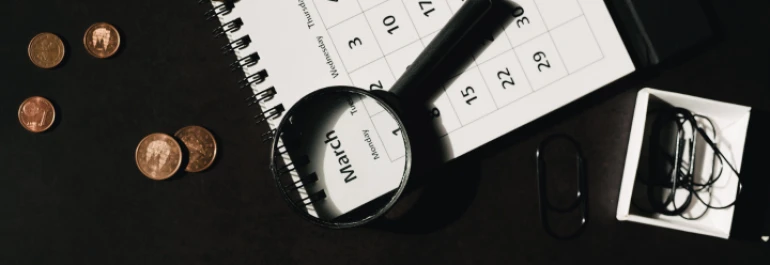  Calendario sobre fondo negro, con lupa sobre el mes de marzo, con monedas y clips alrededor 