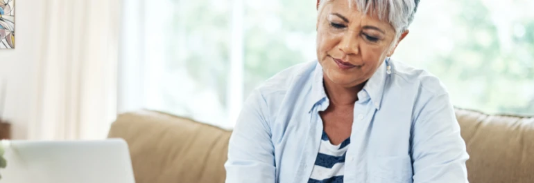  Persona mayor concentrada trabajando en una computadora portátil en casa. 