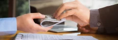  Dos manos entregando dinero sobre una mesa con documentos y un boli 