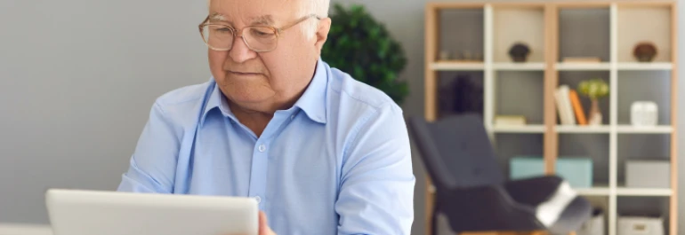 Hombre de tercera edad leyendo en una tablet con una oficina de fondo 