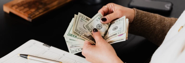  Una persona cuenta billetes mientras está sentada en un escritorio con un cuaderno y un bolígrafo. 