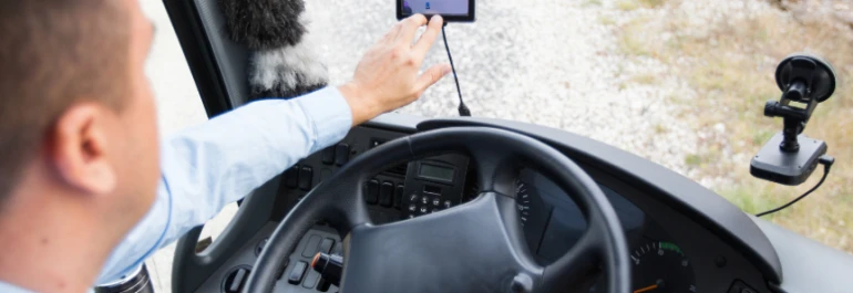  Una persona está en el asiento del conductor de un vehículo, usando un dispositivo móvil montado en el tablero. 