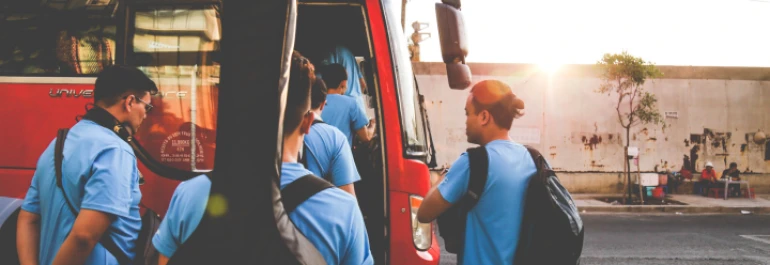  Un grupo de personas sube a un autobús rojo al atardecer. 
