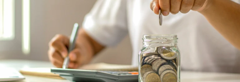  Persona haciendo cálculos e introduciendo monedas de Euro en un bote 