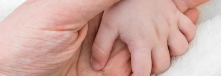  Una mano adulta sosteniendo la mano de un bebé. 