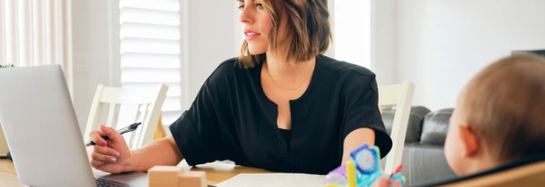  Una persona trabaja en una computadora mientras cuida a un bebé. 