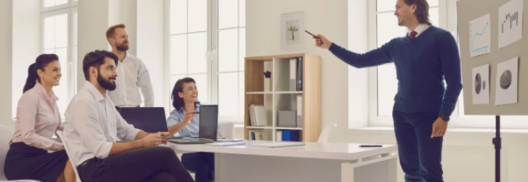  Una persona está presentando información en una reunión frente a varias personas sentadas. 