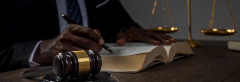  Una persona está escribiendo en un libro mientras hay un mazo y una balanza en la mesa. 