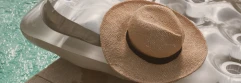  sombrero de paja con cinta negra descansando sobre un colchón inflable plateado junto a una piscina de agua turquesa. La escena transmite una sensación de verano, descanso y relax junto al agua 