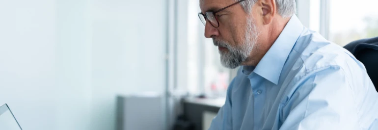  Hombre mayor con barba y gafas trabajando en una computadora. 