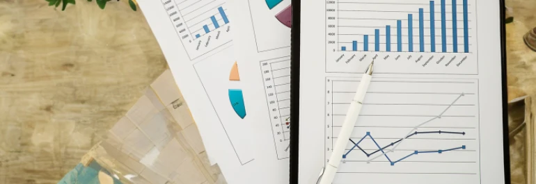  Documentos con gráficos y tablas de datos están sobre una mesa con un bolígrafo. 