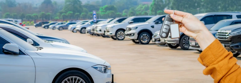  Una persona sostiene llaves frente a una fila de autos estacionados. 