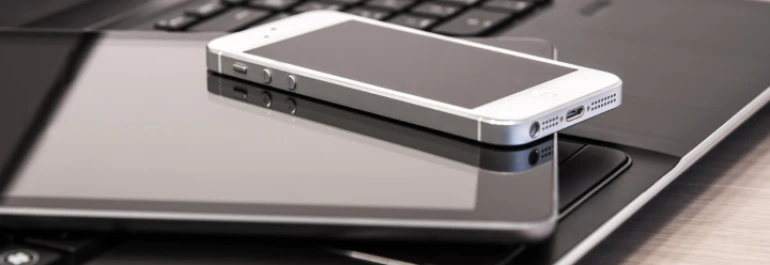  Un smartphone blanco descansa sobre una tablet negra y una laptop. 