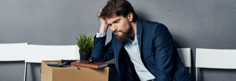  Un hombre de aspecto preocupado se sienta junto a una caja de artículos personales. 