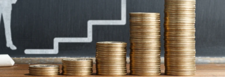  Varias pilas de monedas en aumento frente a un fondo de pizarra con un diagrama de escalera. 