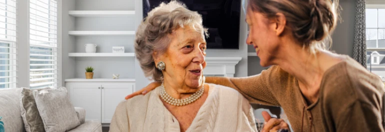  Una mujer mayor y una mujer más joven están sonriendo y conversando en una sala de estar. 
