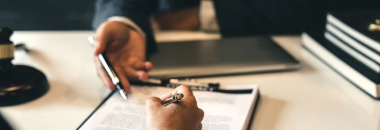  Dos personas revisan y firman documentos frente a un escritorio. 
