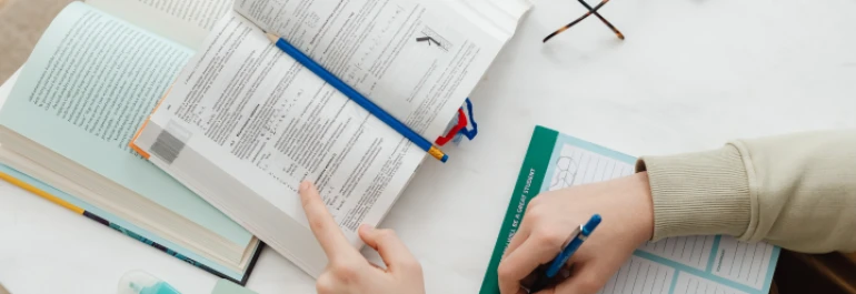  Una persona está estudiando con un libro abierto y tomando notas en un cuaderno. 