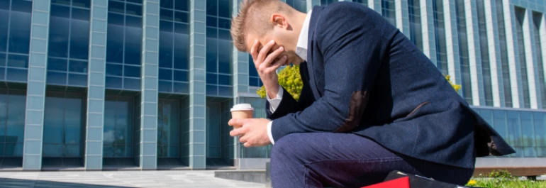  Un hombre sentado afuera de un edificio parece preocupado mientras sostiene una taza de café. 