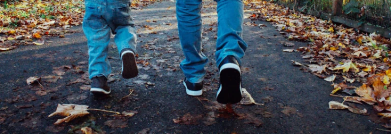  Niño y adulto caminando de espaldas por sendero con hojas en el suelo 