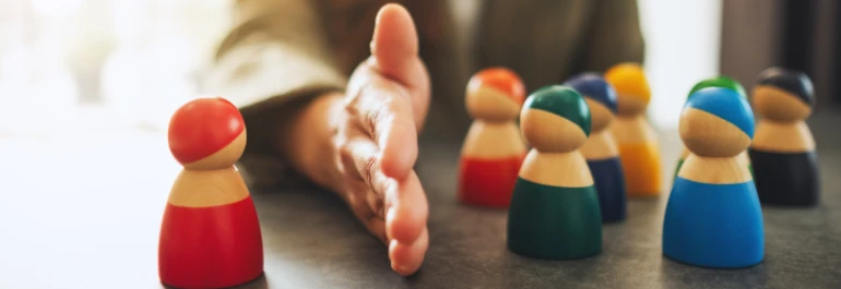  Una mano separa una figura de madera roja de un grupo de figuras de colores. 
