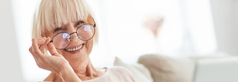  Una mujer mayor sonriente con gafas, sentada en un espacio iluminado. 