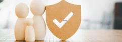  Figuras de madera representando una familia junto a un escudo con un símbolo de verificación. 