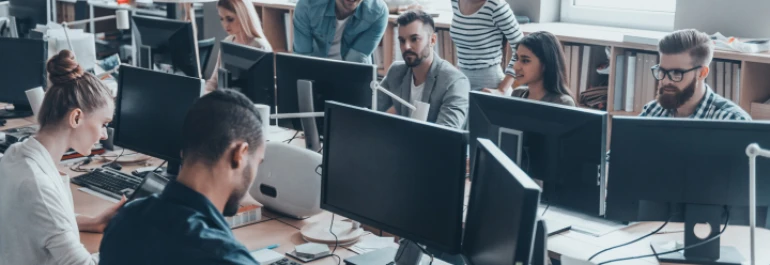  Un grupo de personas trabaja en una oficina con computadoras sobre escritorios compartidos. 
