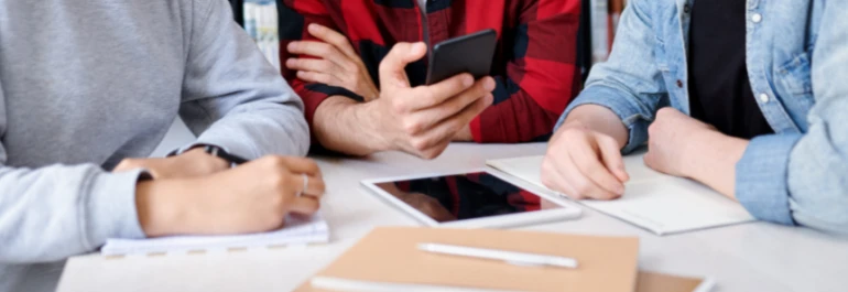  Tres personas están reunidas alrededor de una mesa con cuadernos, un teléfono y una tablet. 