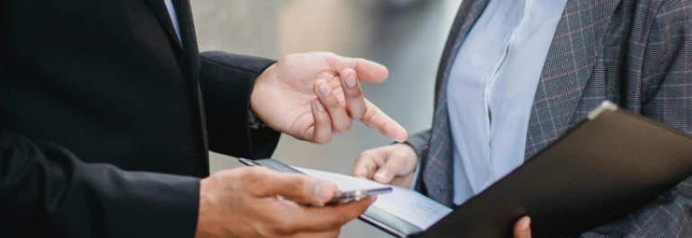  hombre con traje gesticulando frente a mujer con americana que está sosteniendo un portafolios 