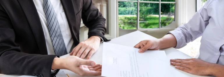  Dos personas en una oficina revisan un documento frente a una ventana. 