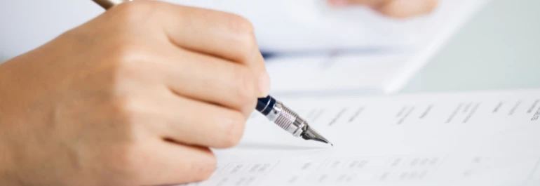  Una mano sostiene una pluma mientras escribe en un documento. 