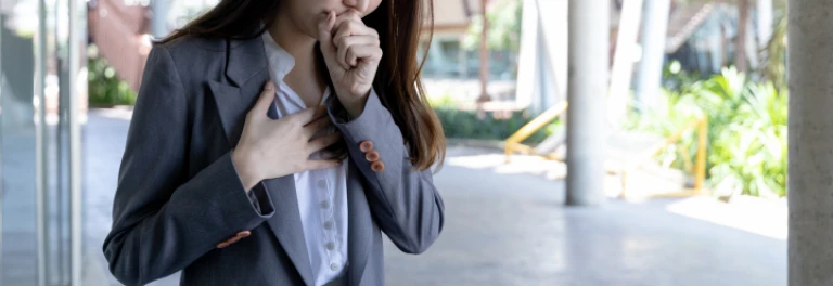  Mujer de traje tosiendo, sujetándose el pecho con una mano, mientras se cubre la boca con la otra 