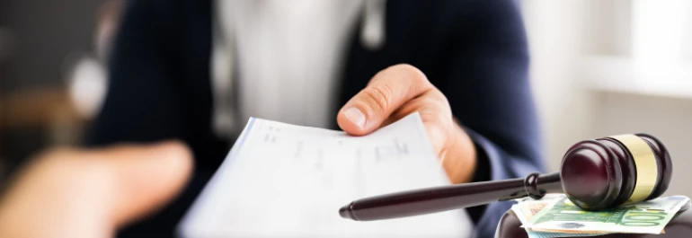  Una persona entregando un cheque y un martillo de juez sobre billetes de euros. 