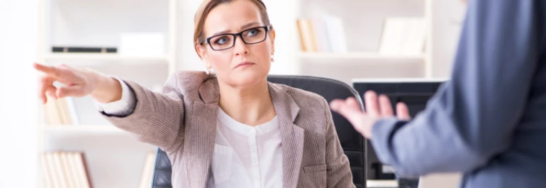  Una mujer en una oficina señala hacia otra persona mientras parece estar hablando. 