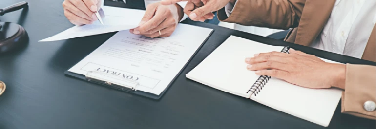  Dos personas revisan y discuten un contrato sobre una mesa. 